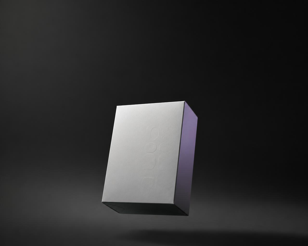 Estuche farmacéutico minimalista color hueso sobre fondo obsidiana, con un único reflejo violeta en una de sus caras
